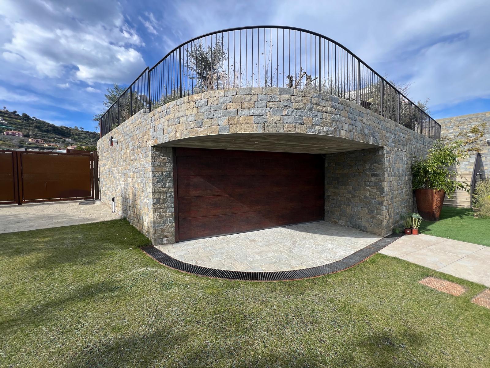 Portone da garage sezionale con finitura effetto legno integrato nella facciata in pietra di una villa sulla Riviera di Ponente - Lanzoni Filippo Serramenti
